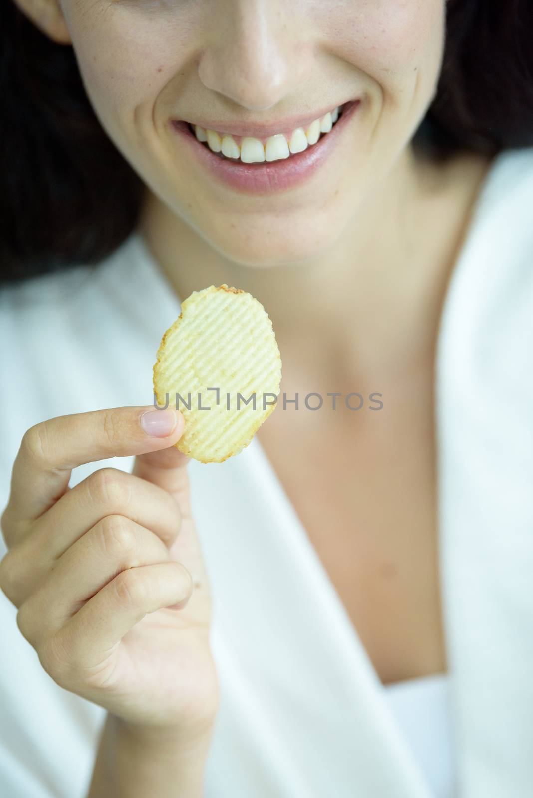 A beautiful woman wearing a towel and a white bathrobe has to eat a snack potato with happy and relaxing on the bed at a condominium in the morning.