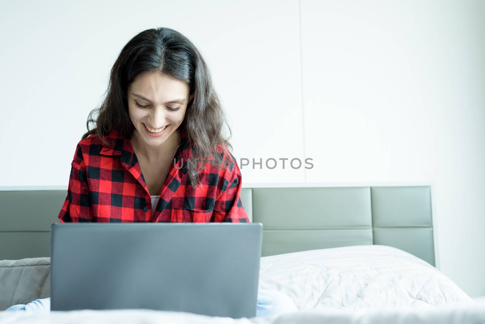 Beautiful woman working on a laptop with smiling and sitting on the bed at a condominium in the morning.