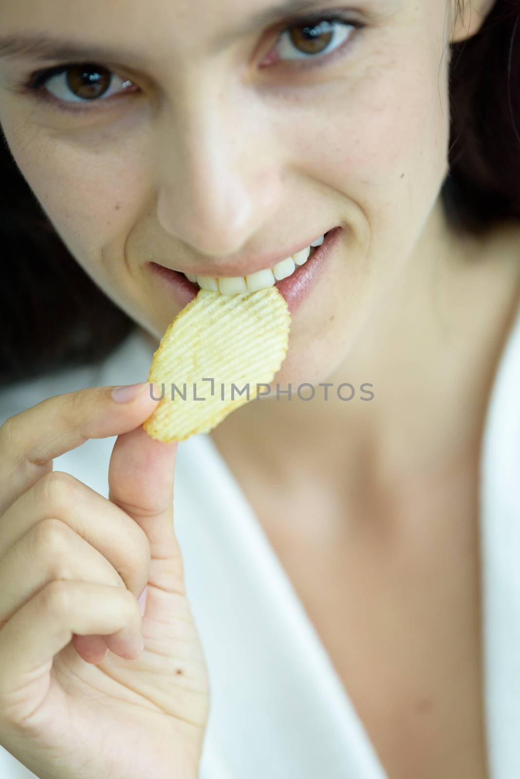 A beautiful woman wearing a towel and a white bathrobe has to eat a snack potato with happy and relaxing on the bed at a condominium in the morning.