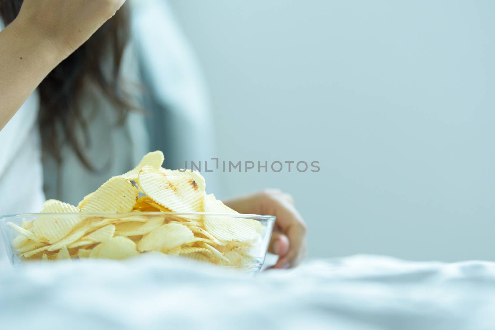 A beautiful woman eating snack potato and playing laptop with lying down on the bed and happiness at a condominium in the morning.