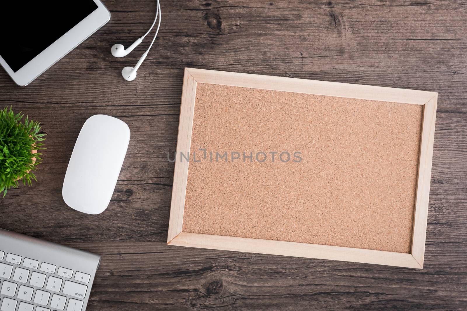 The office desk flat lay view with keyboard, mouse, tree, office pin board and earphone on wood texture background.