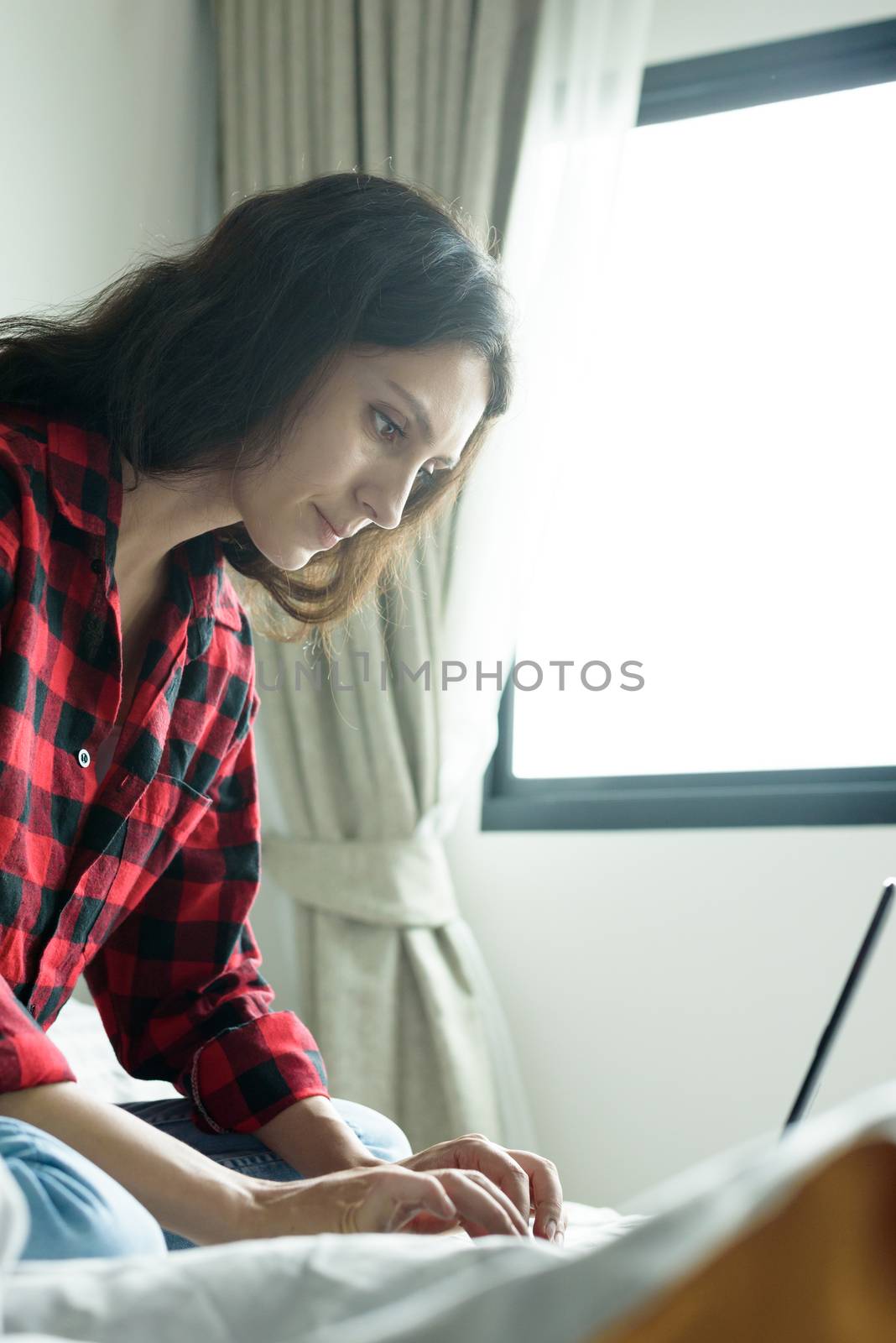 Beautiful woman working on a laptop with smiling and sitting on the bed at a condominium in the morning.