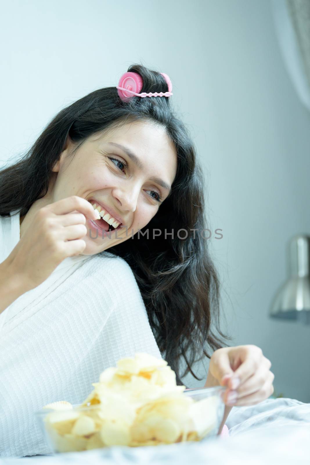 A beautiful woman eating snack potato and playing laptop with lying down on the bed and happiness at a condominium in the morning.