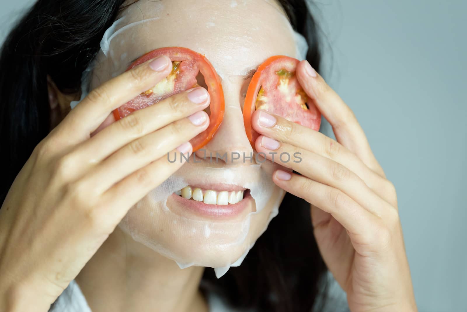 A beautiful woman wearing a towel and a white bathrobe has mask on face-covering eyes with sliced tomatoes with happy and relaxing on the bed at a condominium in the morning.