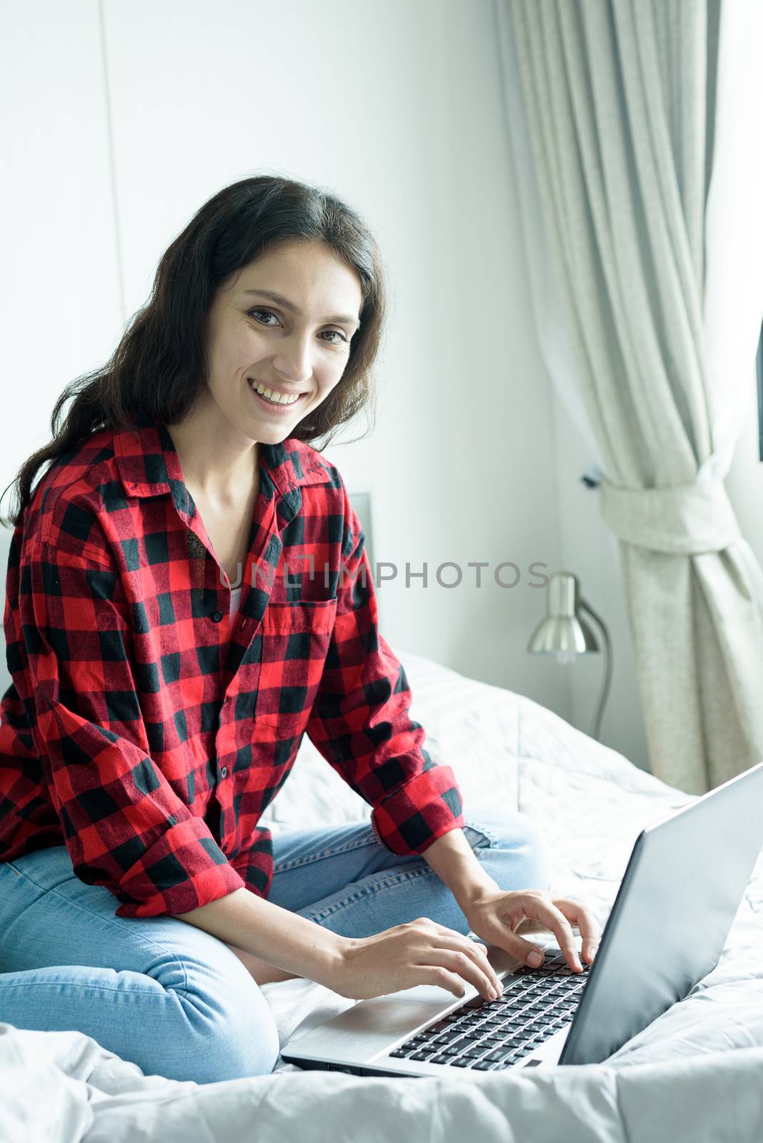 Beautiful woman working on a laptop with smiling and sitting on the bed at a condominium in the morning.