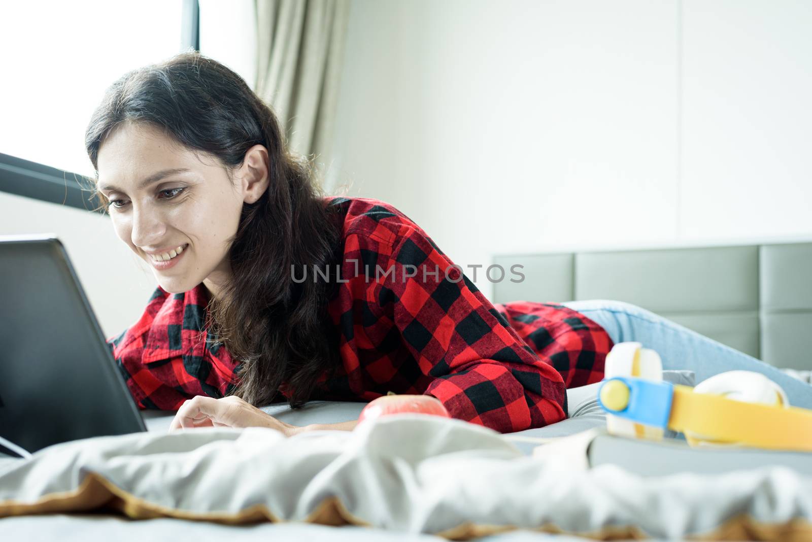 Beautiful woman working on a laptop and lying down on the bed at by animagesdesign