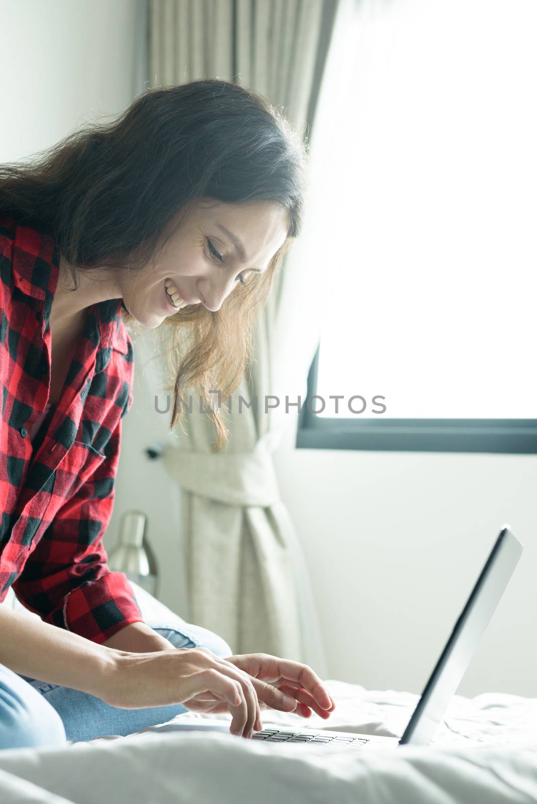 Beautiful woman working on a laptop with smiling and sitting on the bed at a condominium in the morning.