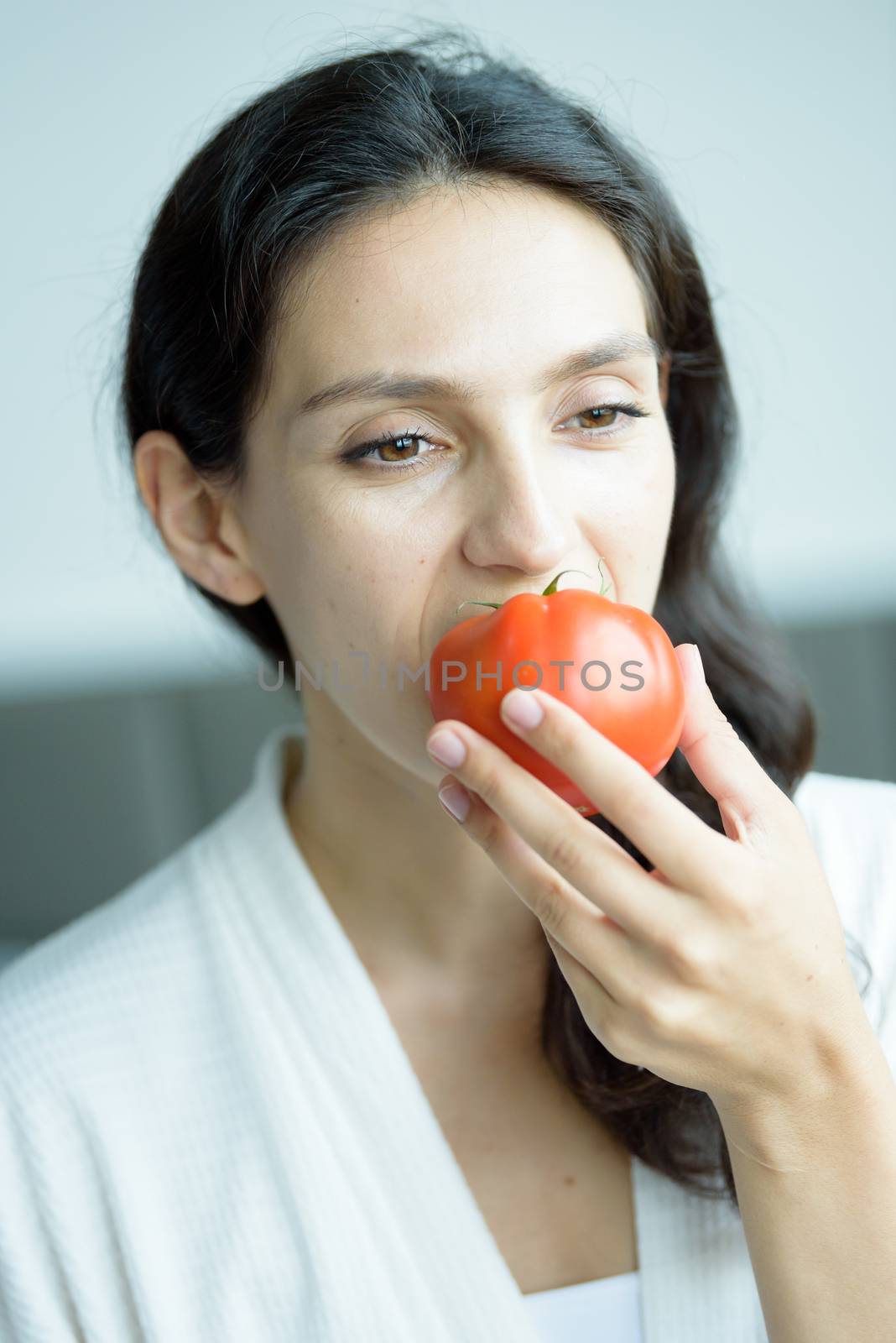 A beautiful woman wearing a towel and a white bathrobe has to prepare to eat tomato with happy and relaxing on the bed at a condominium in the morning.