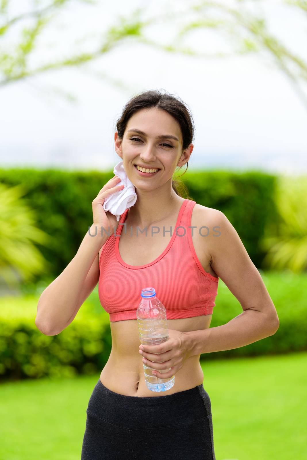 Beautiful woman runner has tired and rest for drinking water and a white towel to wipe her face after running in the garden.