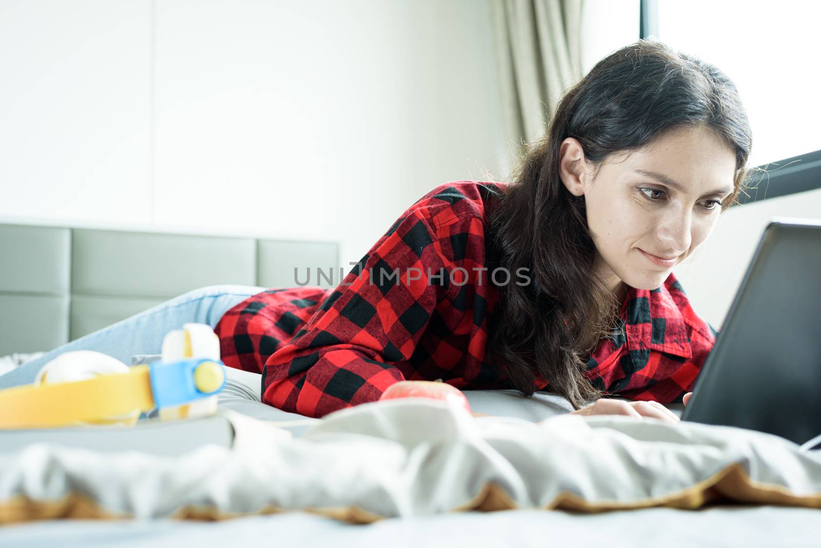 Beautiful woman working on a laptop and lying down on the bed at a condominium in the morning.