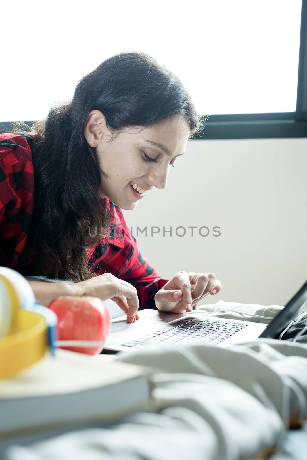 Beautiful woman working on a laptop and lying down on the bed at a condominium in the morning.