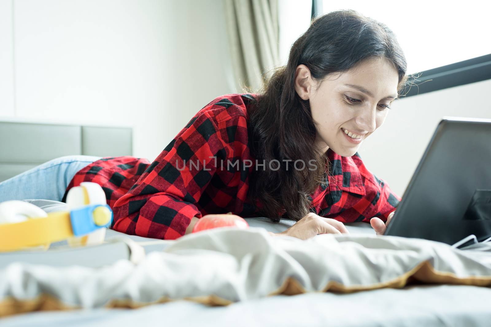 Beautiful woman working on a laptop and lying down on the bed at a condominium in the morning.