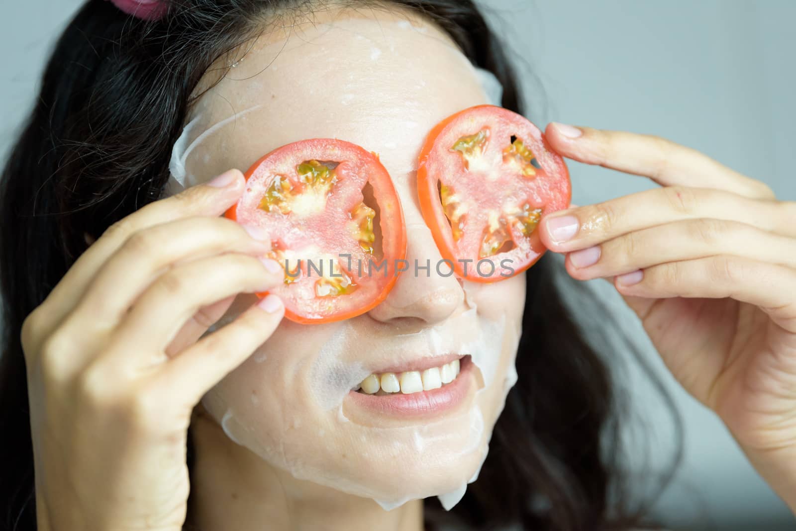 A beautiful woman wearing a towel and a white bathrobe has mask on face-covering eyes with sliced tomatoes with happy and relaxing on the bed at a condominium in the morning.