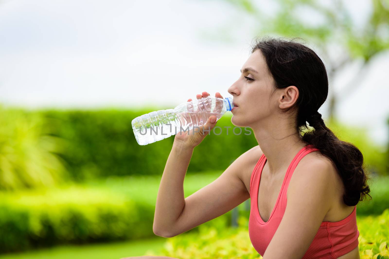 Beautiful woman runner has tired and rest for drinking water after running in the garden.