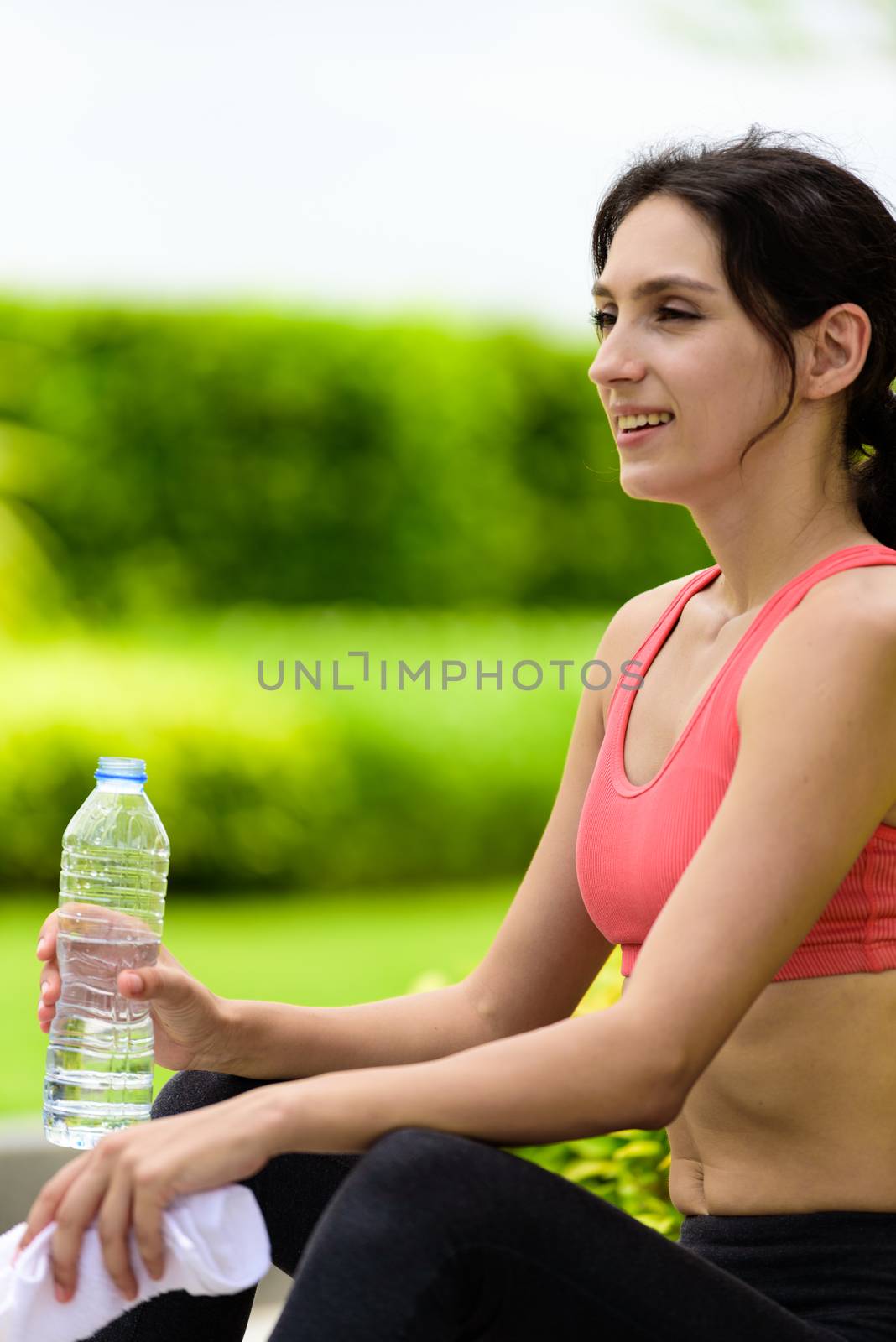 Beautiful woman runner has tired and rest for drinking water and a white towel to wipe her face after running in the garden.