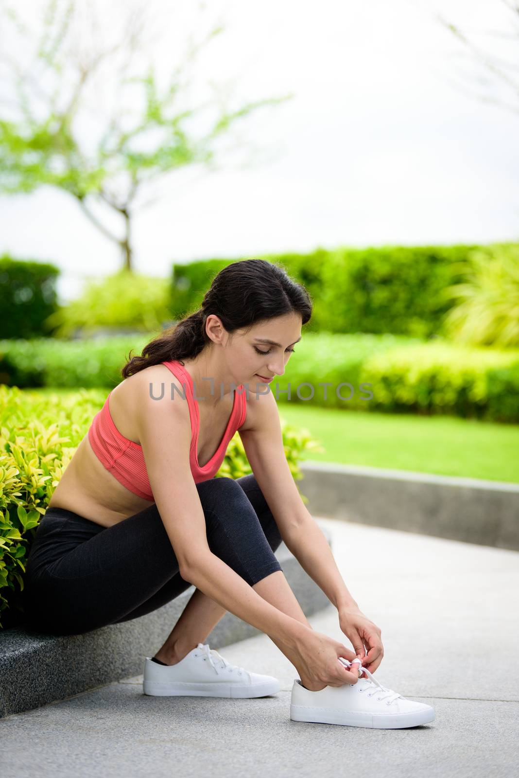 Beautiful woman runner has to tie white shoelaces in the garden.