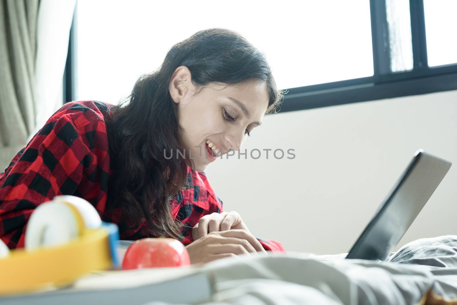 Beautiful woman working on a laptop and lying down on the bed at a condominium in the morning.