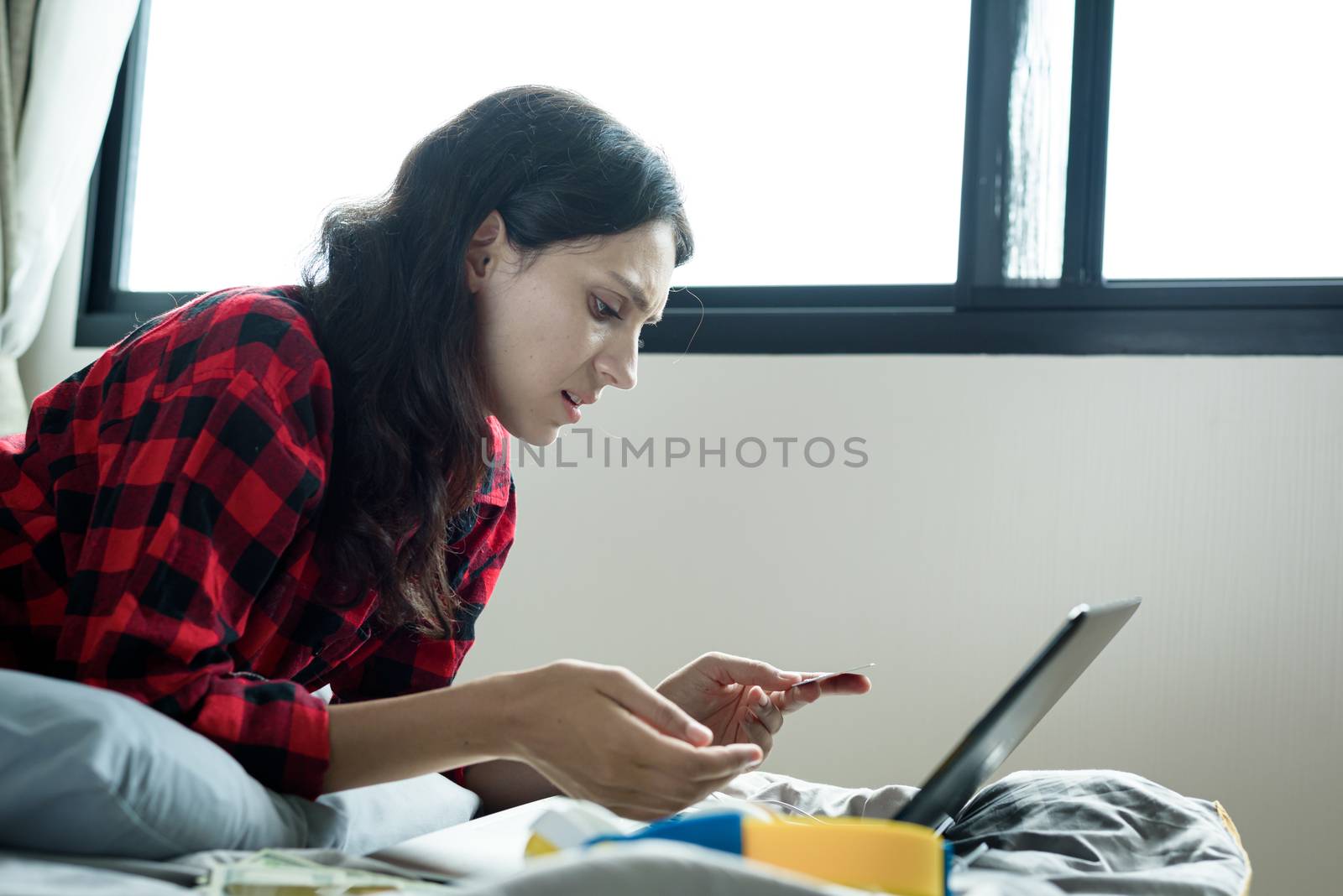 A beautiful woman has lain down on the bed at a condominium and shopping online on a laptop by the credit card with unhappy and worried in the morning.