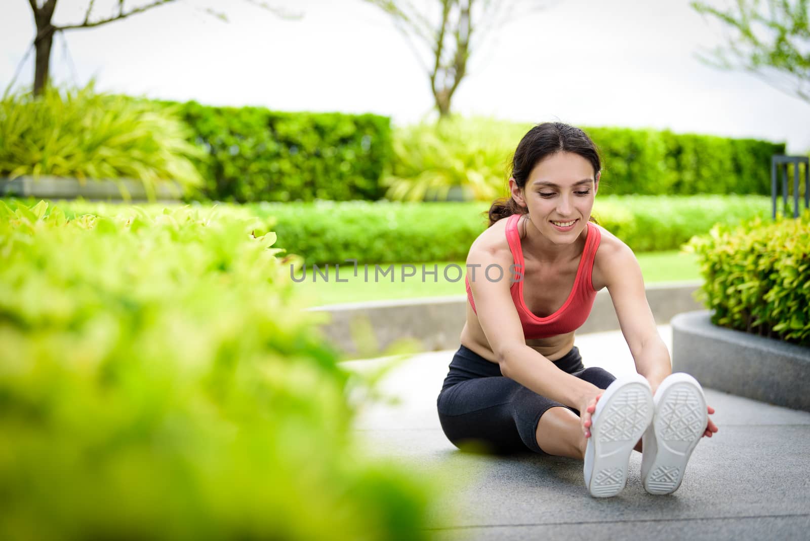 Beautiful woman runner has to warm up with stretching in the gar by animagesdesign