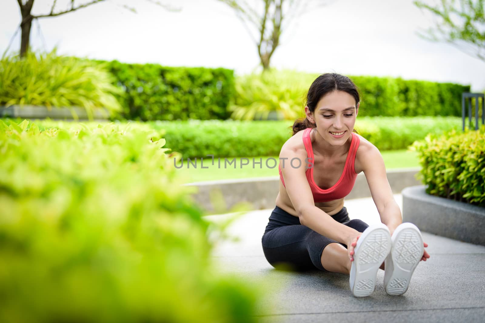 Beautiful woman runner has to warm up with stretching in the garden.