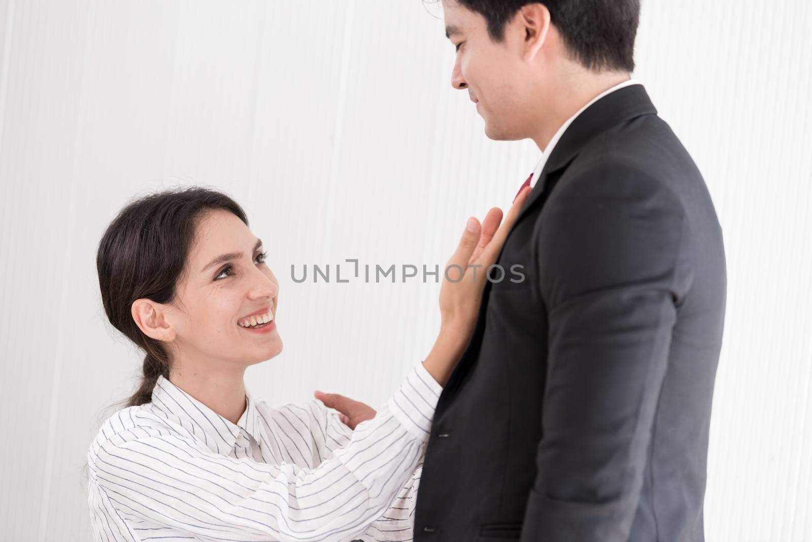 Wife tying red necktie to her husband in the office with smiling and happy.