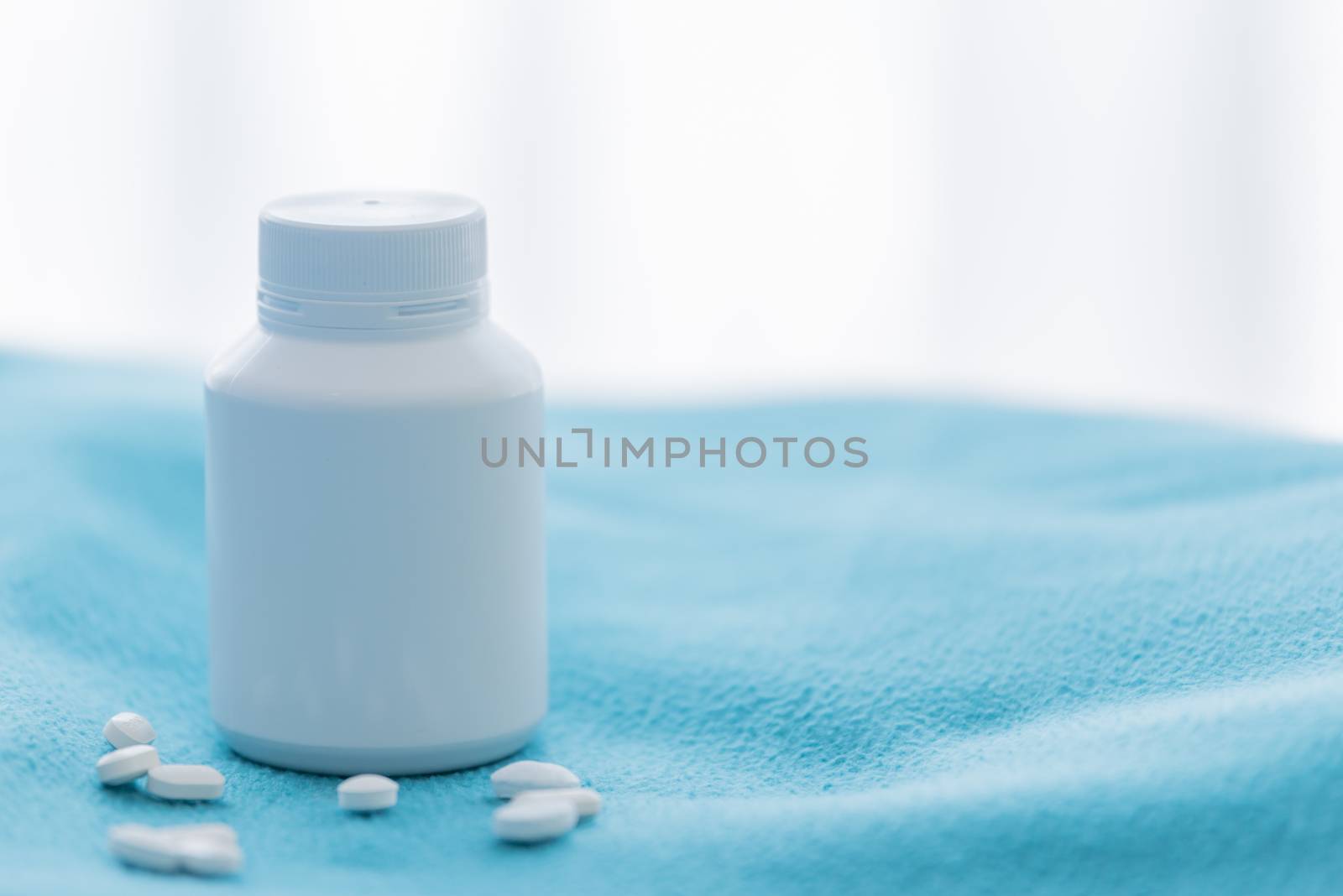 A white medicine bottle and medicine drop on the green bed sheet.