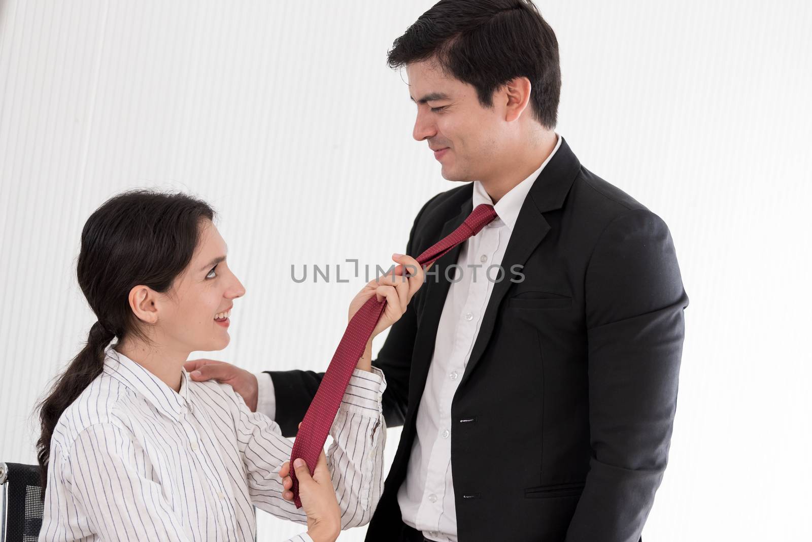 Wife tying red necktie to her husband in the office with smiling and happy.