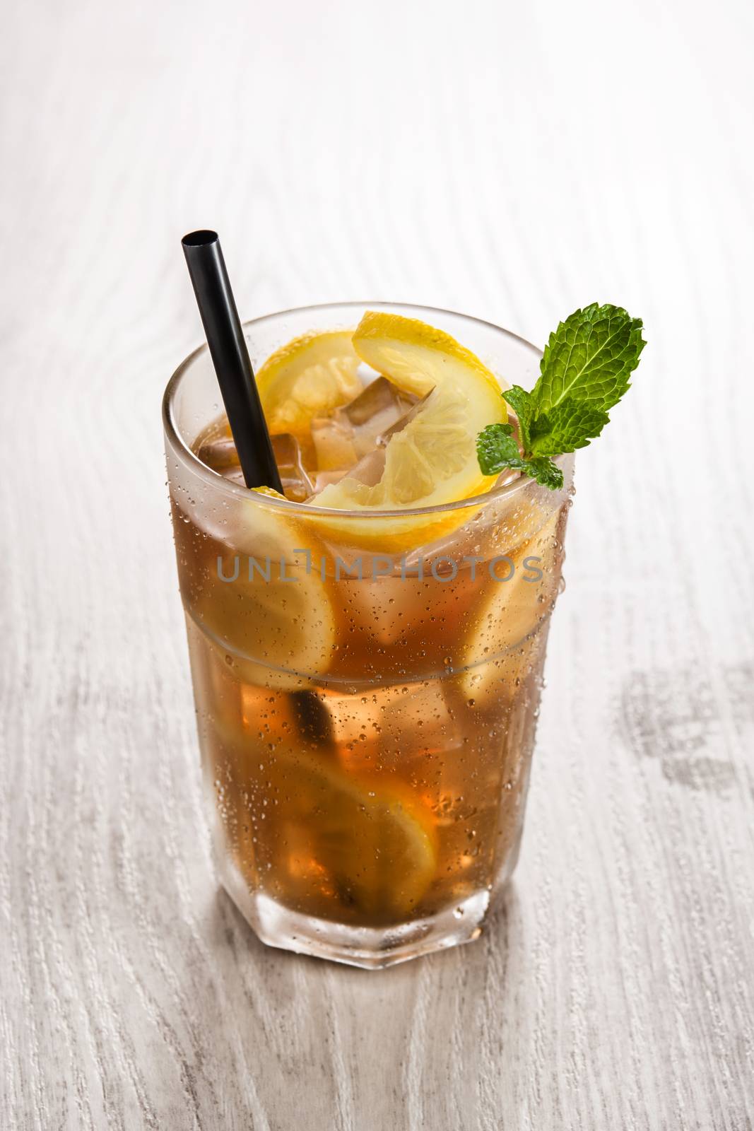 Iced tea drink with lemon in glass on white wooden table