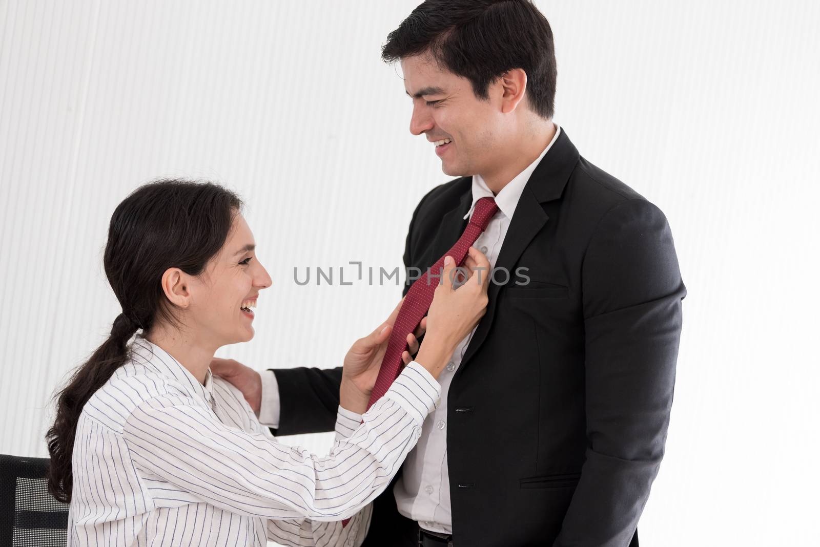 Wife tying red necktie to her husband in the office with smiling by animagesdesign