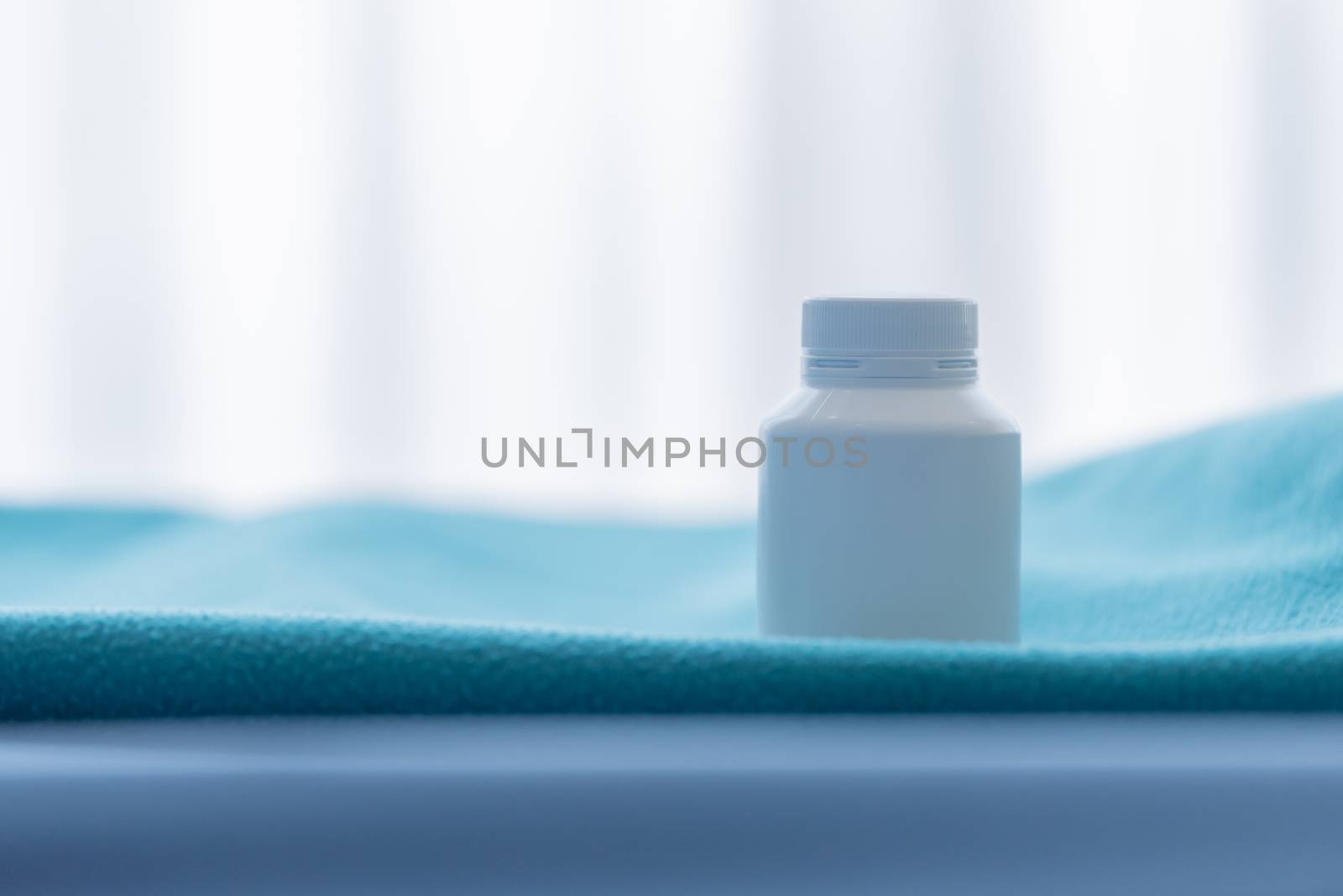 A white medicine bottle on the green bed sheet.