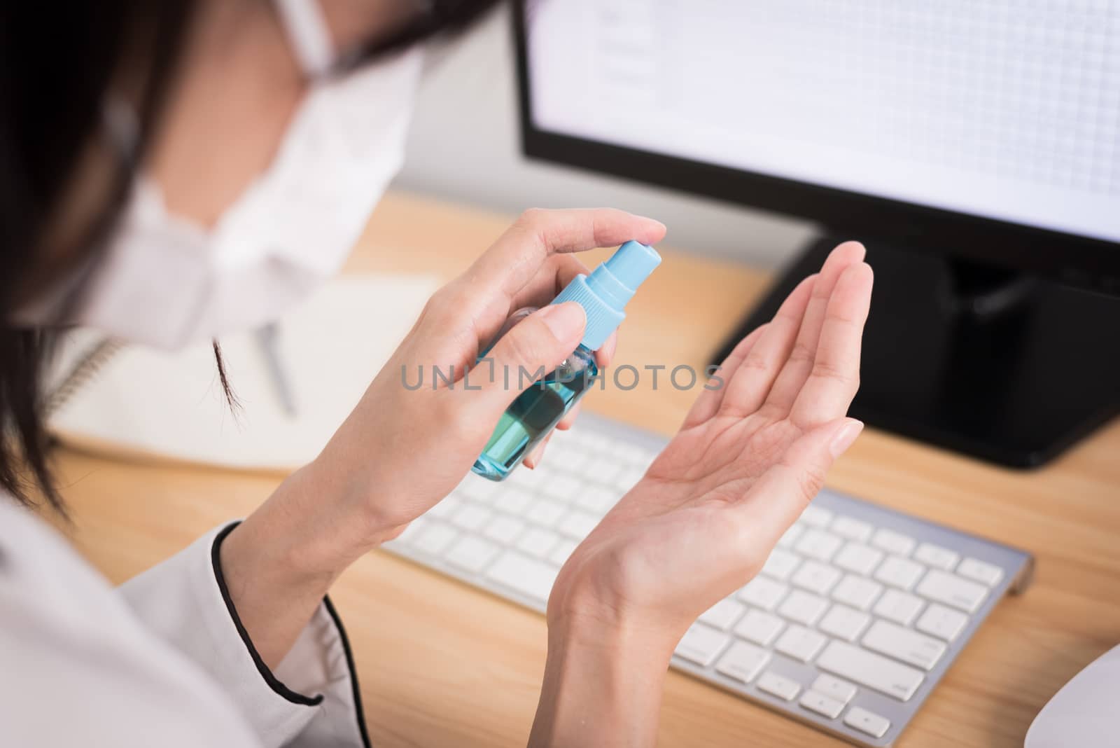 A beautiful Asian businesswoman wearing a mask does cleaning hands with cleaner gel to protect COVID-19 before start working from home with safety and happiness.