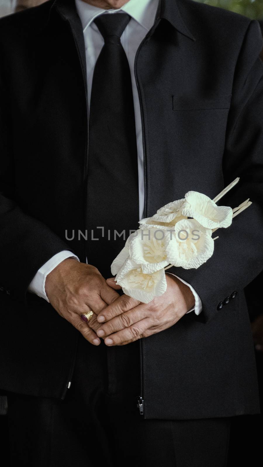 An old man with a white flower stands to mourn the deceased.