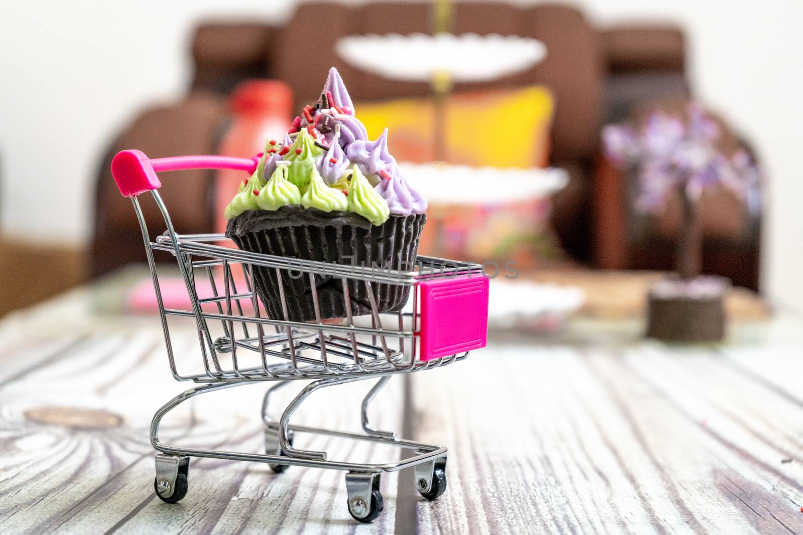 Beautifully iced cupcake with purple frosting and black chocolate base on a shopping cart on a wooden floor with blurred out background. Shows hobbies and skills people are leanring in the coronavirus pandemic