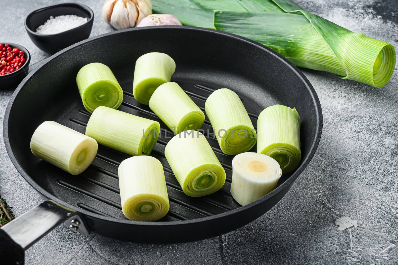 Raw chopped Leeks on grill pan uncooked with herbs ingredients , on textured grey background side view selective focus with space for text