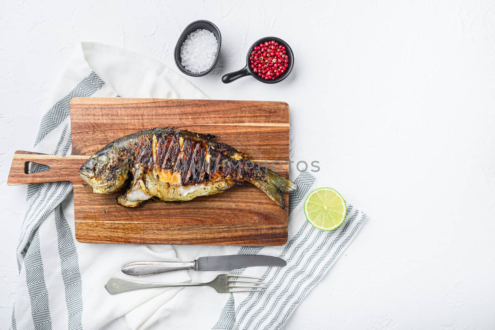 Grilled sea bream or dorado raw fish on chopping board with ingredients over textured white background, top view with space for text
