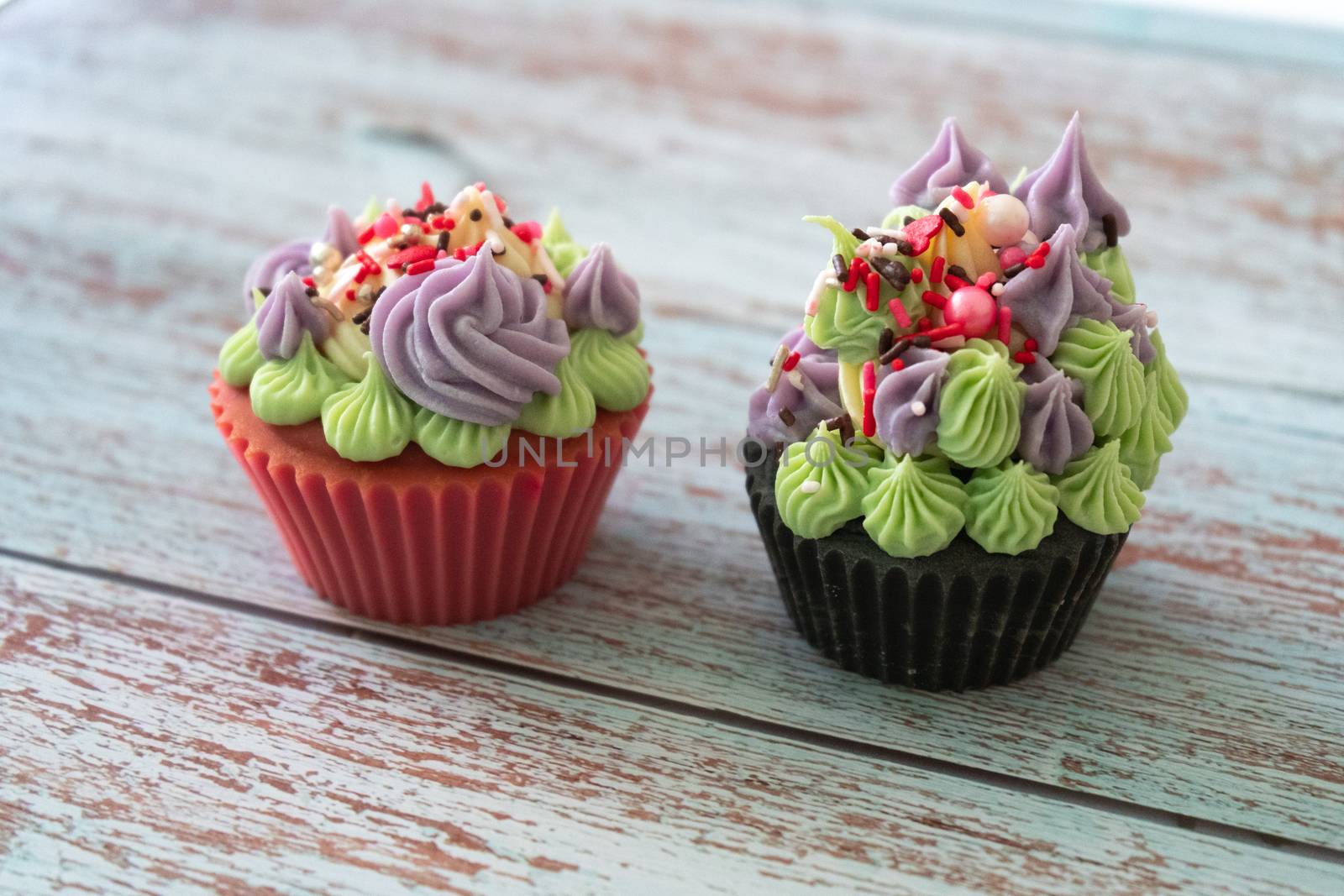 Beautiful cupcakes soap with purple and green icing on pink and dark chocolate base with candy sprinkles placed on a wooden backdrop . Shows the hobbies skills and small businesses that people are working on during the lockdown