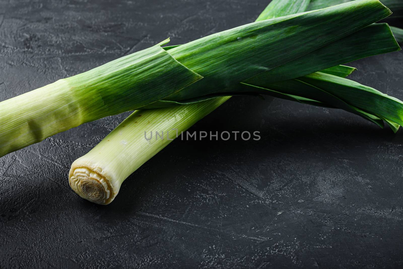 raw green Leek onion on black textured background, side view. by Ilianesolenyi