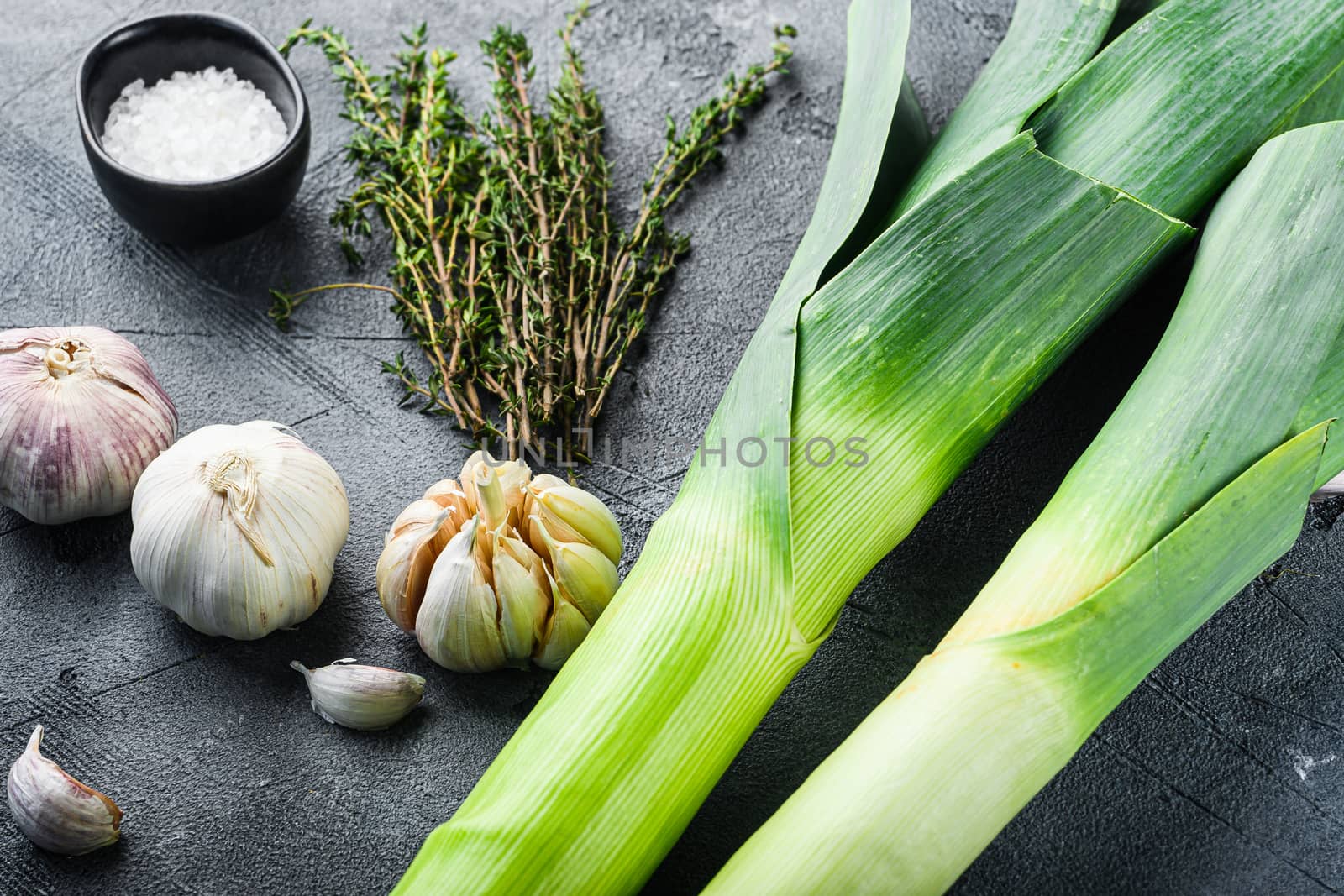Leek stalks with herbs ingredients for coocing Braised Leeks, on grey textured table side view