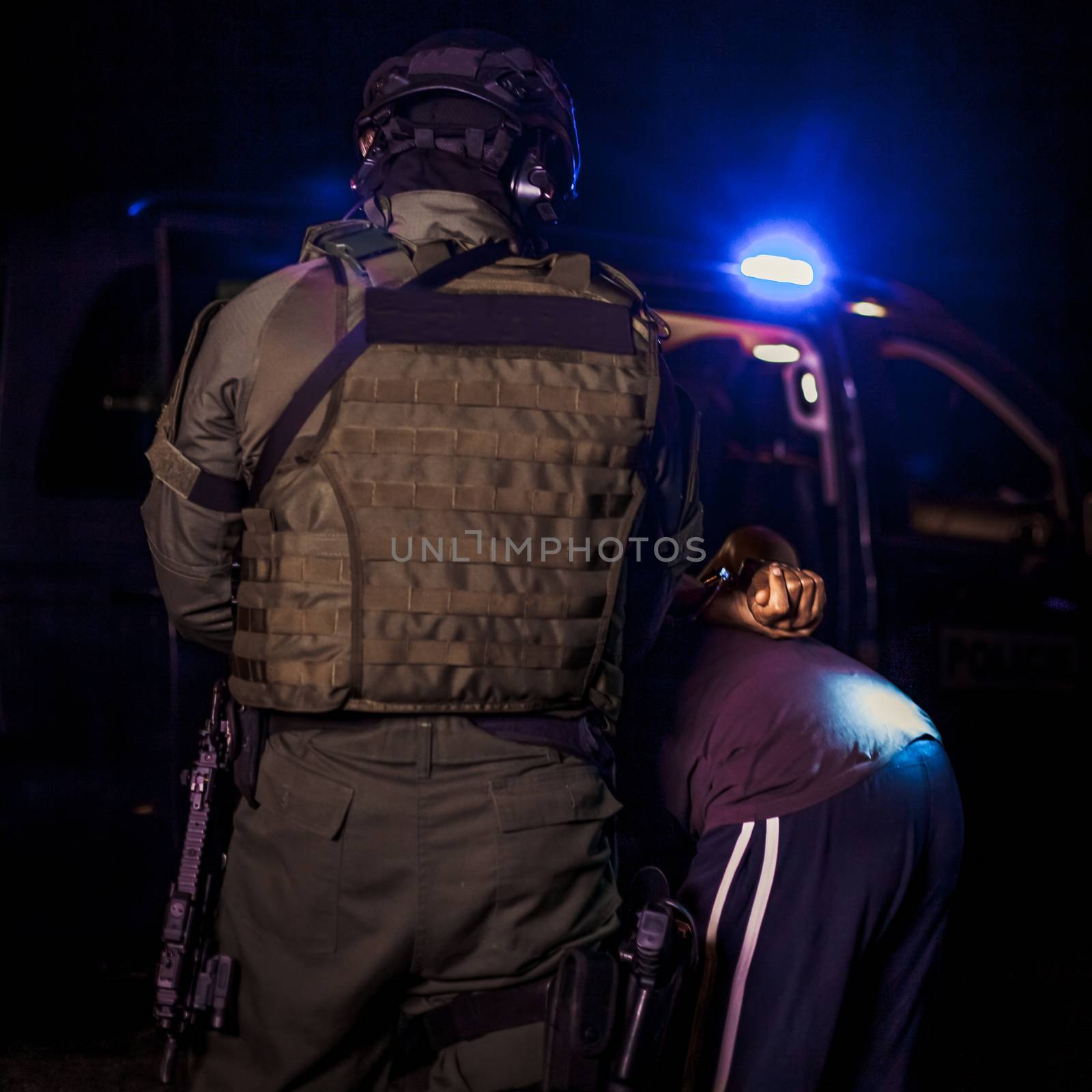 A police officer puts handcuffs on a criminal's hands during an arrest. Police car with flashing lighthouses by Edophoto