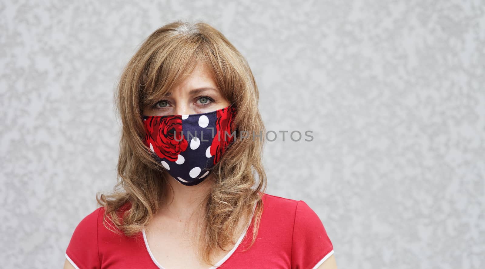 Girl in a protective mask against coronavirus on a background of a gray concrete wall. Primary red color