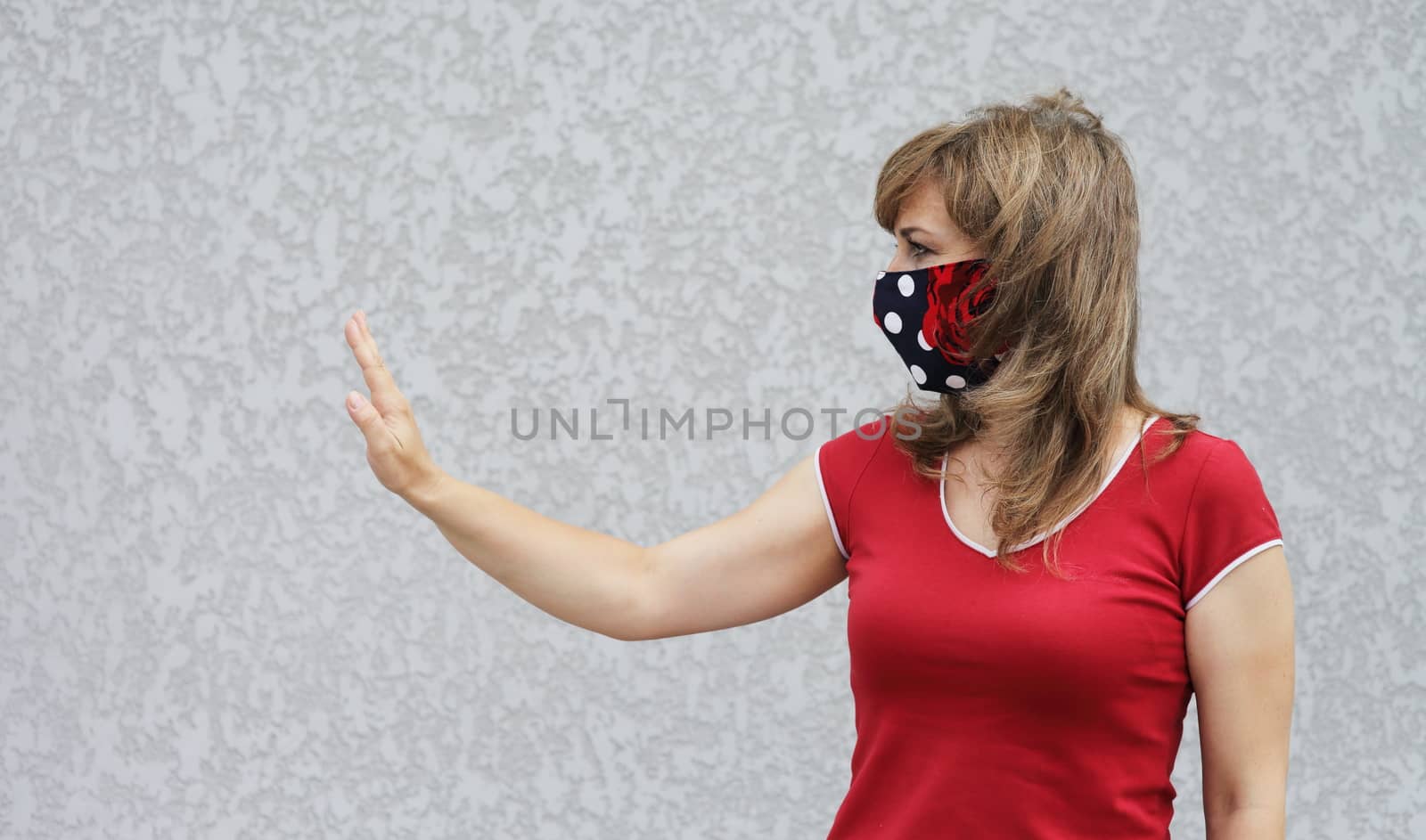 Girl in a protective mask against coronavirus on a background of a gray concrete wall. Primary red color