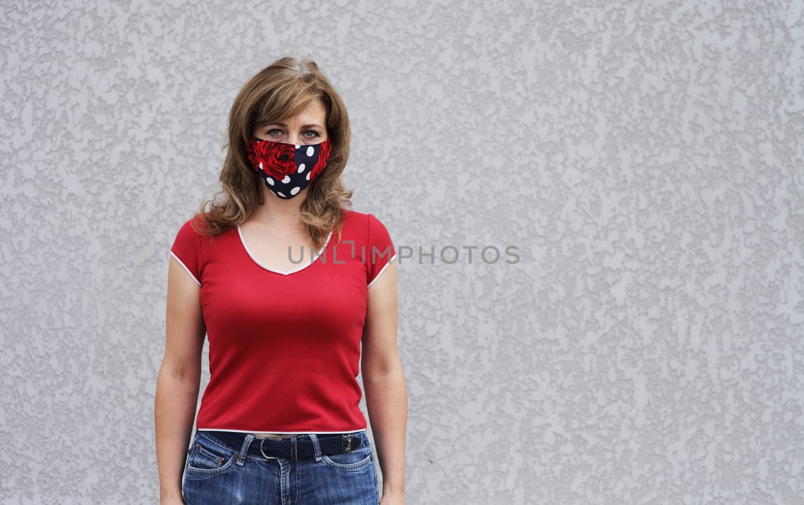 Girl in a protective mask against coronavirus on a background of a gray concrete wall. Primary red color