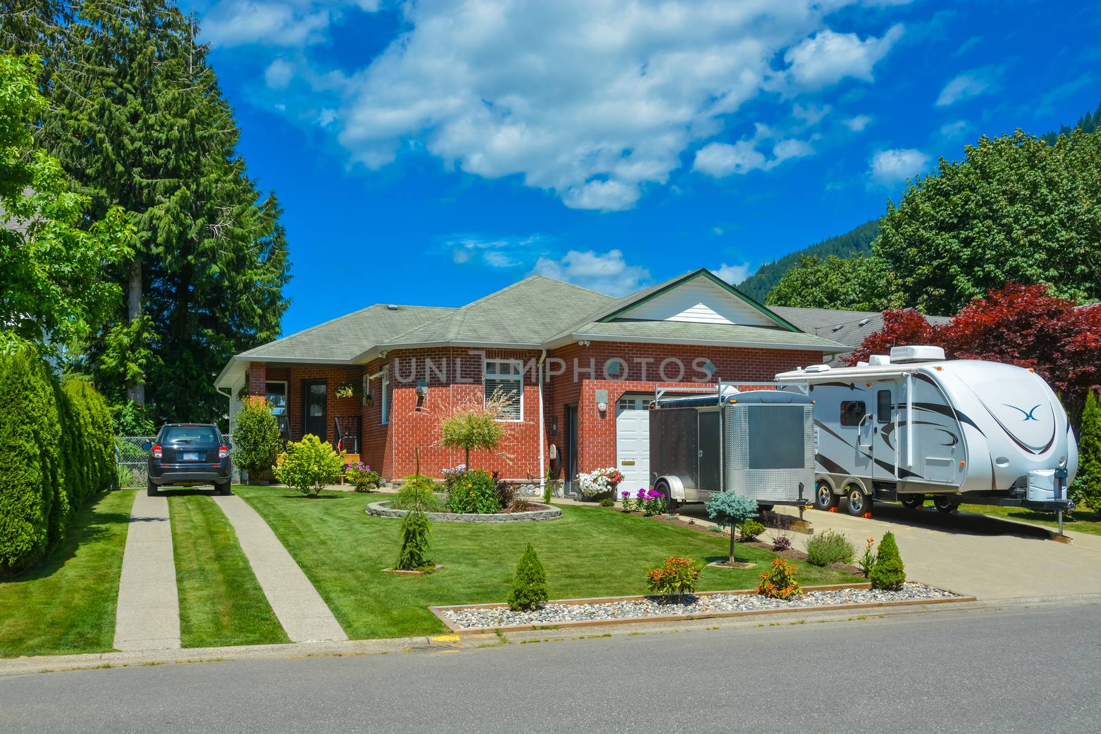 Family house with traced driveway and parked car on it. Residential house with RV parked in front on blue sky background