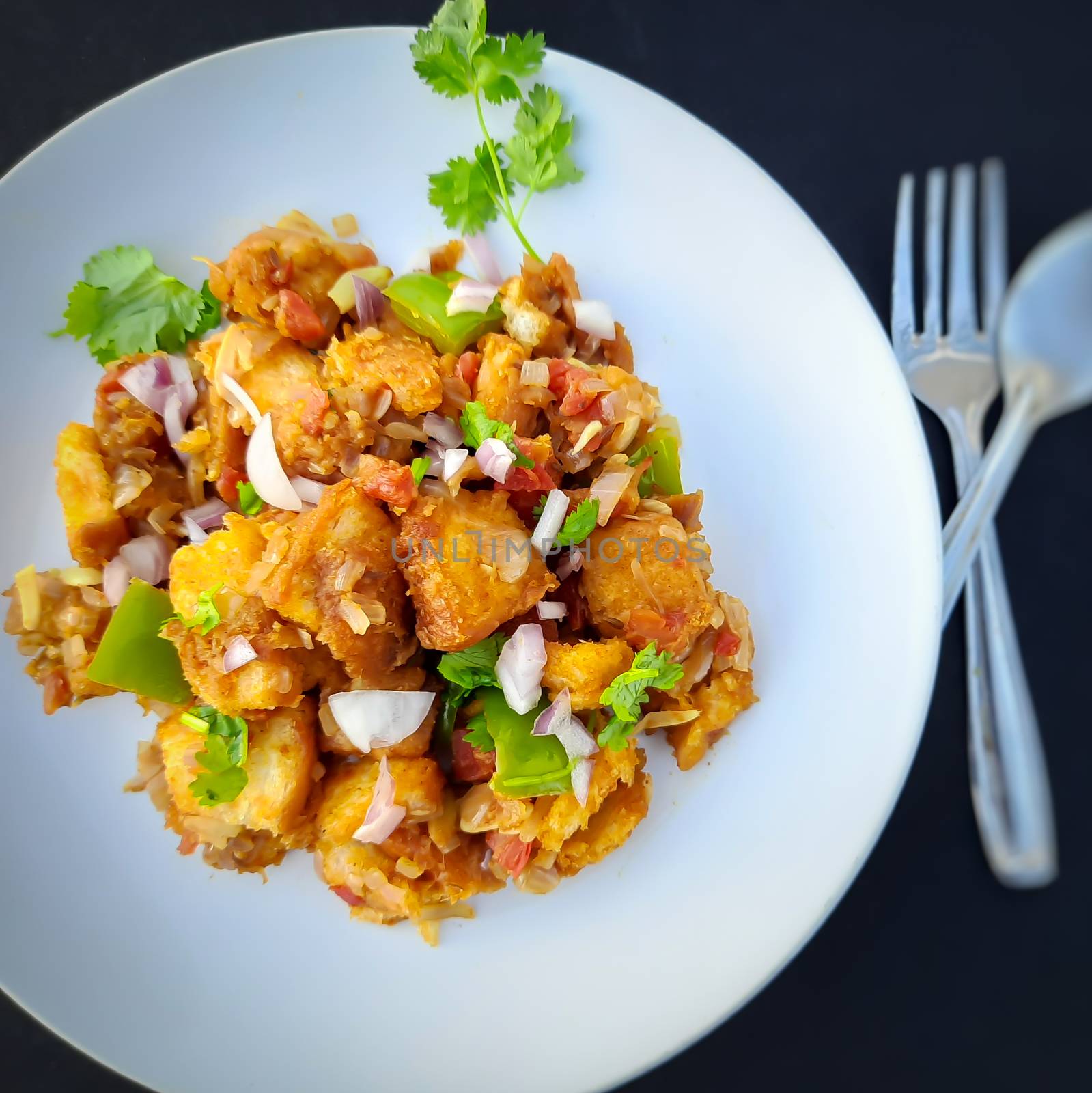 Indian style bread manchurian prepared with capsicum and onion spreaded on it and plated beautifully in white plate with spoons