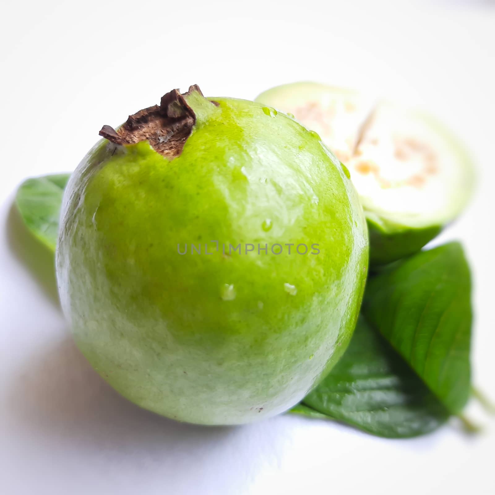 Green color guava with cut pieces and leaves arranged beautifully with white background plated with leaves and good for health and skin and Help Lower Blood Sugar Levels