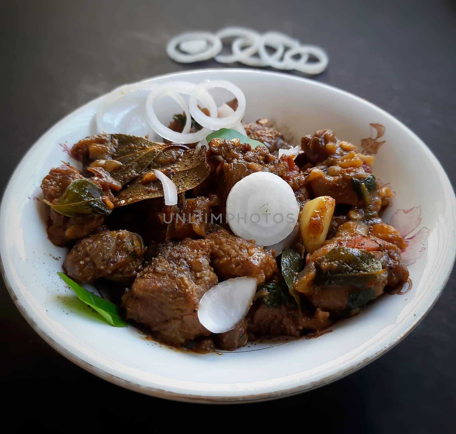 Delicious Indian style spicy pepper mutton placed beautifully in white bowl plated with onions and curry leaves and good for bones