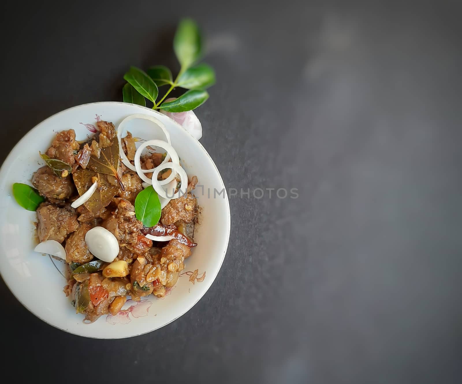 Delicious Indian style spicy pepper mutton placed beautifully in white bowl plated with onions and curry leaves and good for bones