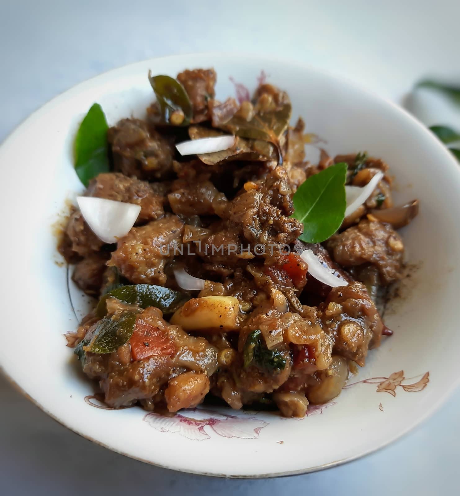 Delicious Indian style spicy pepper mutton placed beautifully in white bowl plated with onions and curry leaves and good for bones