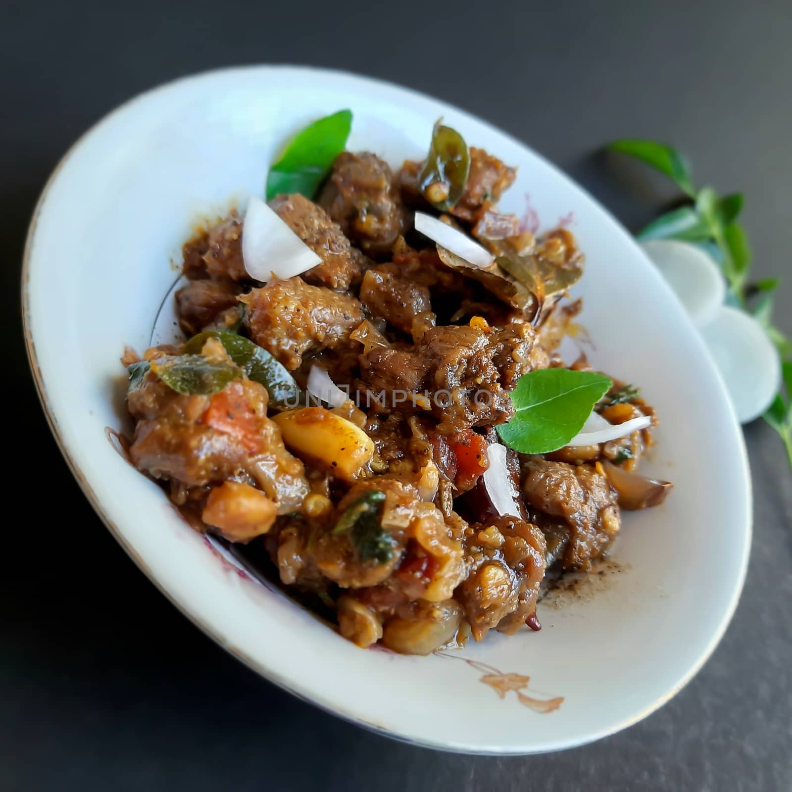 Delicious Indian style spicy pepper mutton placed beautifully in white bowl plated with onions and curry leaves and good for bones