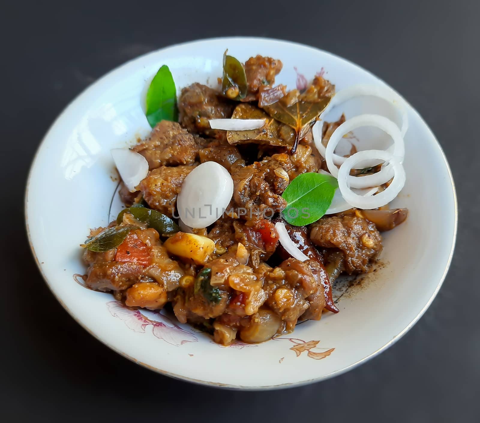 Delicious Indian style spicy pepper mutton placed beautifully in white bowl plated with onions and curry leaves and good for bones